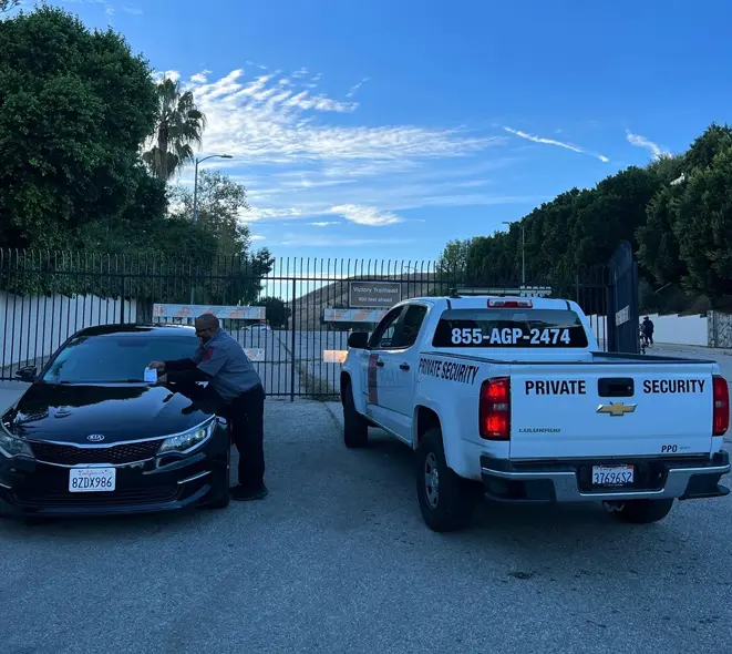 A man standing next to two cars in front of a fence.